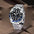 Reloj GMT negro y azul con brazalete de cinco eslabones, en posición vertical sobre tela