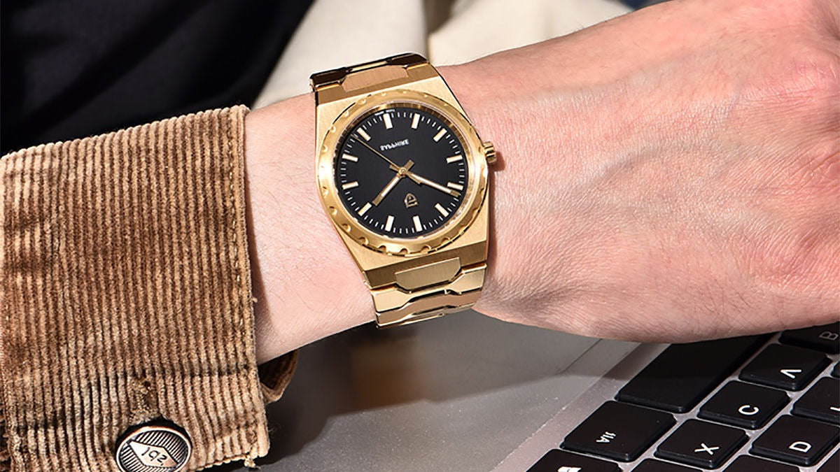Ultra-thin men's watch worn on the wrist beside a laptop, jacket cuff